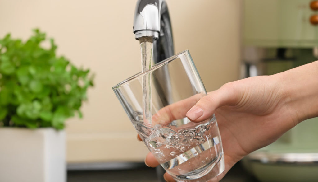 Woman filling glass with fresh water from kitchen faucet
