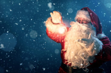 Happy Santa Claus holding glowing christmas ball over defocused